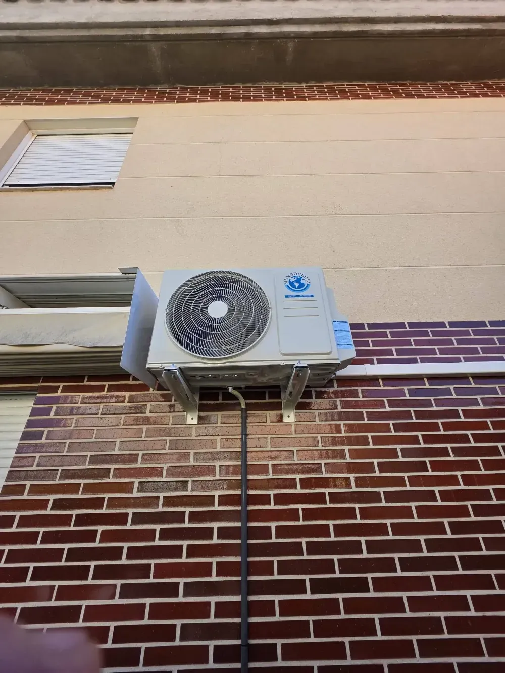 Aire acondicionado de pared en el exterior de un edificio de ladrillo y color beige, debajo de una ventana
