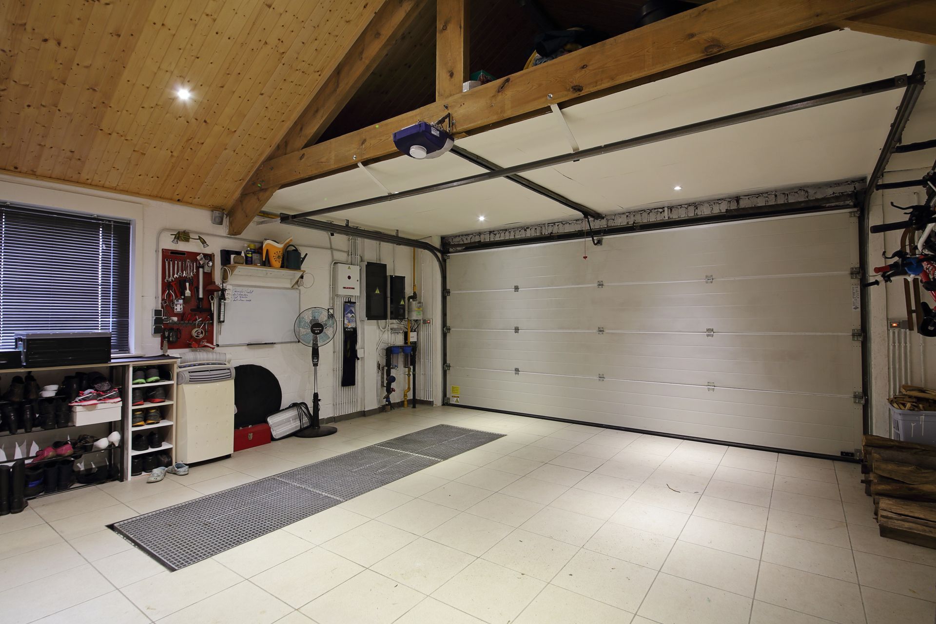 Un garage spacieux et bien éclairé, avec un plafond voûté en bois, un sol carrelé blanc, des étagères de rangement et une grande porte fermée.
