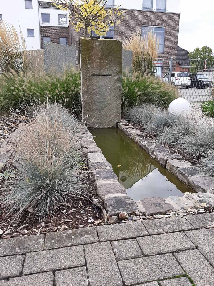 ein kleiner Teich in einem Garten mit einem Gebäude im Hintergrund - Traumgärten Benjamin Biermeyer aus Soest