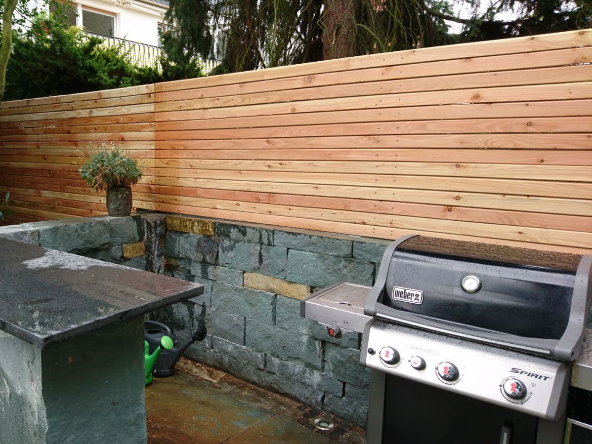 ein Grill steht neben einer Steinmauer und einem Holzzaun - Traumgärten Benjamin Biermeyer aus Soest