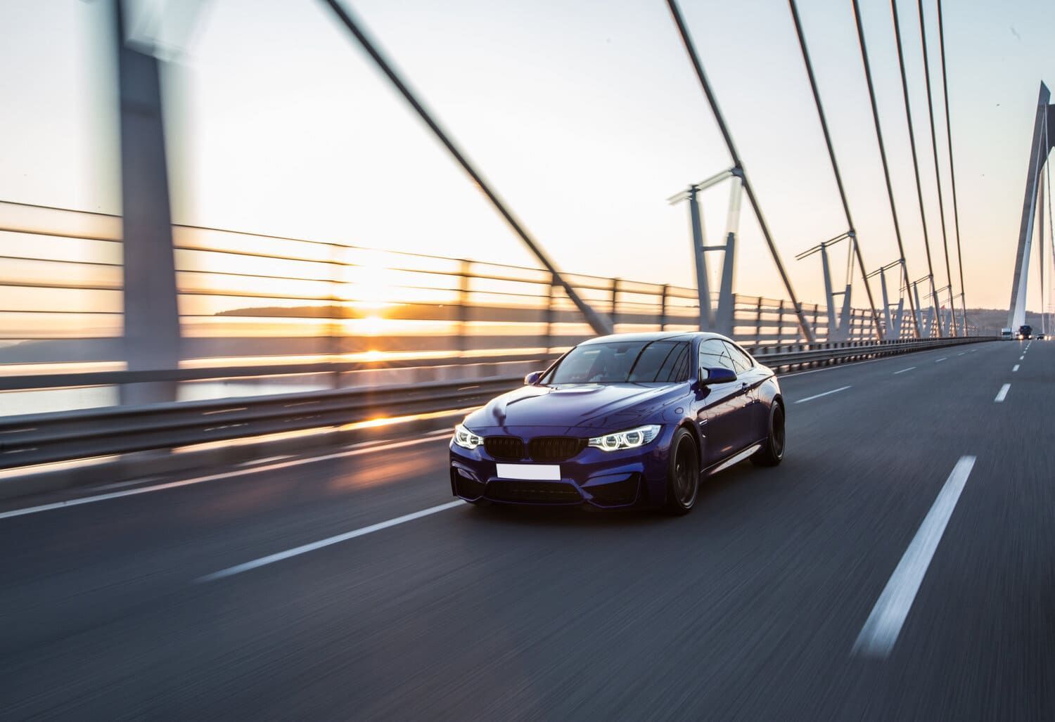 Un coche azul circula por un puente al atardecer.