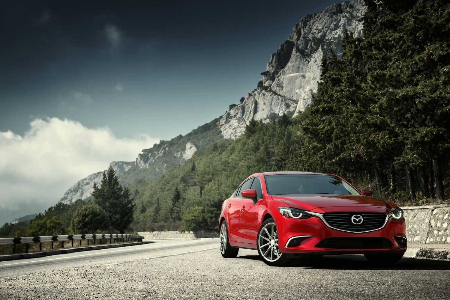 Un Mazda 6 rojo está estacionado al costado de una carretera de montaña.