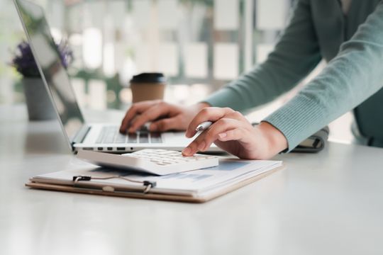 Henkilö laskee laskimella ja kirjoittaa läppärillä