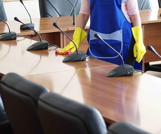 Una mujer está limpiando una mesa de una sala de conferencias con micrófonos.