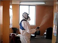 Un hombre con un traje de protección está rociando una habitación con un pulverizador.