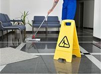 Un hombre está fregando el suelo al lado de una señal de precaución amarilla.