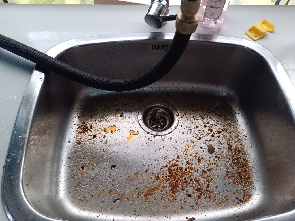 Fregadero de cocina de acero inoxidable sucio con restos de comida y una manguera negra.