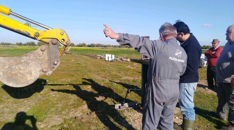 Un grupo de hombres está de pie en un campo con una excavadora amarilla en el fondo.
