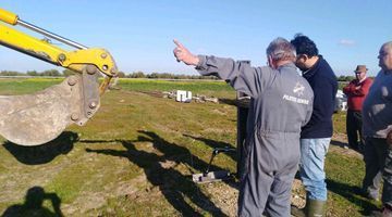 Un grupo de hombres está parado en un campo mirando una excavadora amarilla.