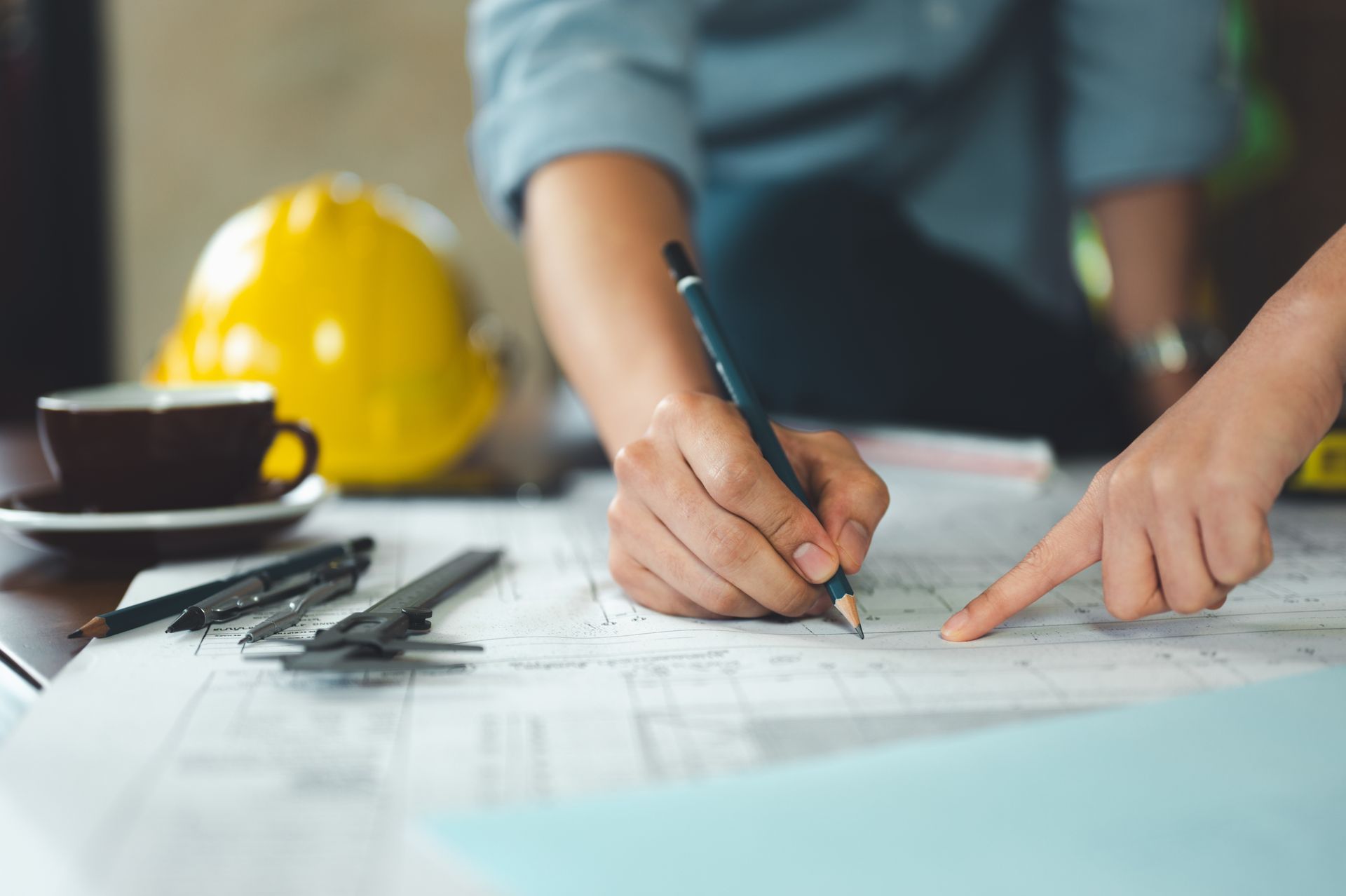 Une personne dessine des plans à une table de chantier, portant un casque jaune et des outils à proximité.