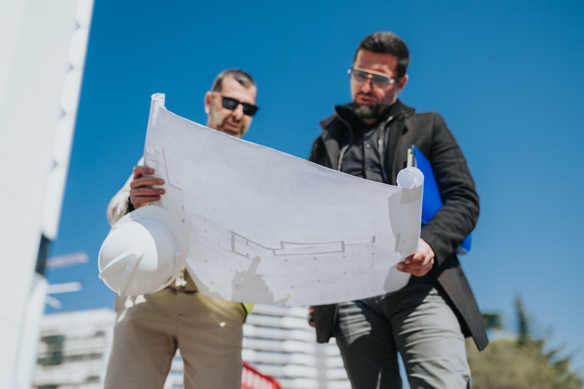 Deux ingénieurs en tenue de sécurité étudient un grand plan à l'extérieur, sur un chantier de construction.