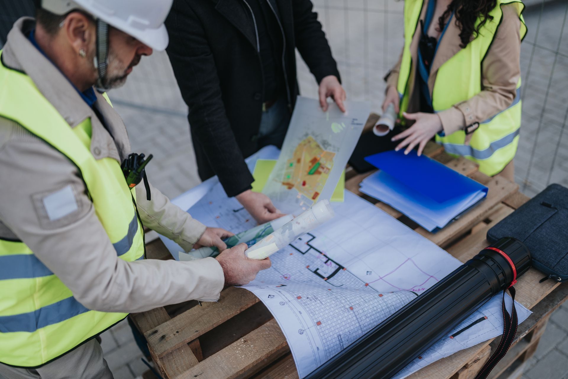 Des ouvriers portant des gilets de sécurité examinent des plans et une carte sur un chantier de construction.