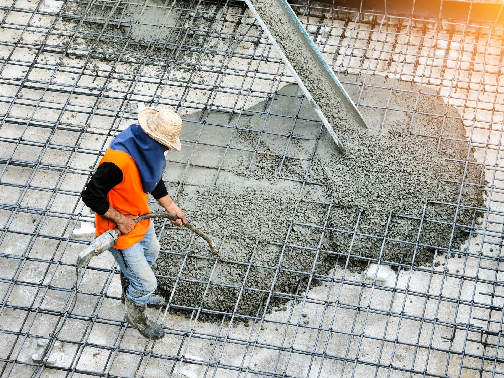 Ouvrier en gilet orange étalant du béton frais sur une armature métallique sur un chantier de construction
