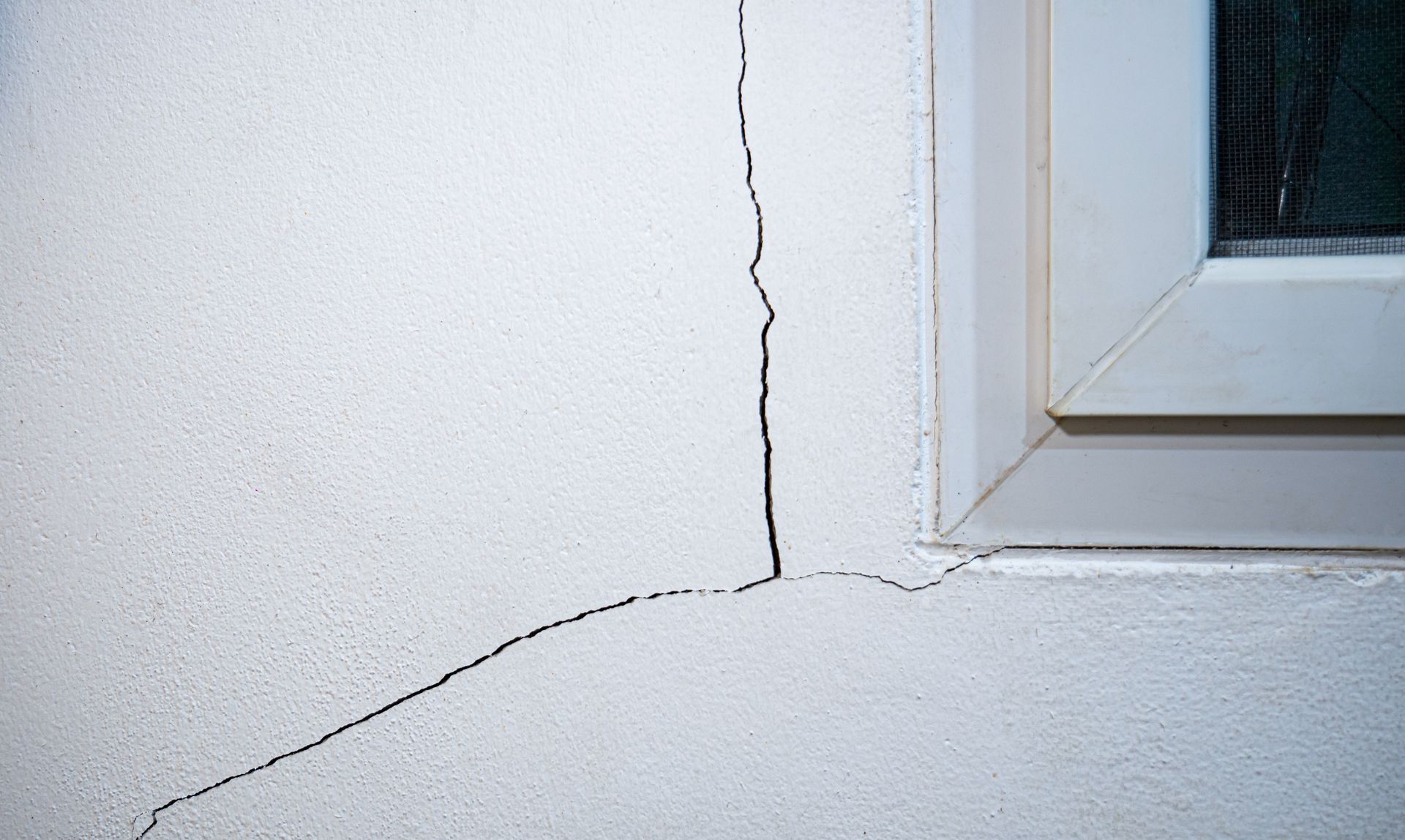 Fissure dans un mur extérieur blanc, près d'un cadre de fenêtre