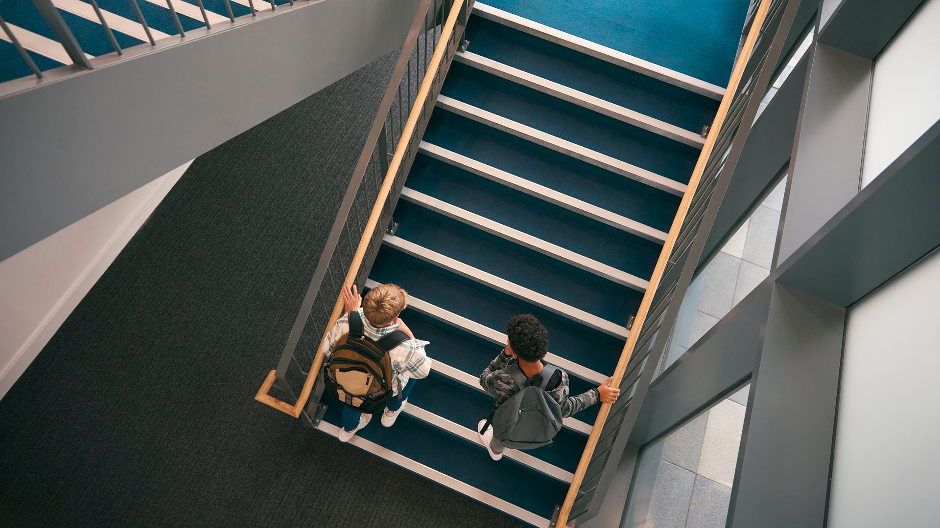 Deux personnes montant un escalier bleu dans un immeuble moderne, vue de dessus.