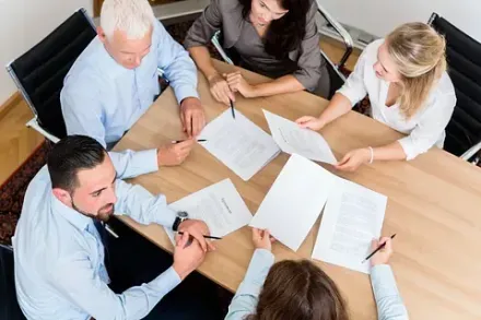 Personas en una mesa revisando documentos, posiblemente en un entorno de oficina.