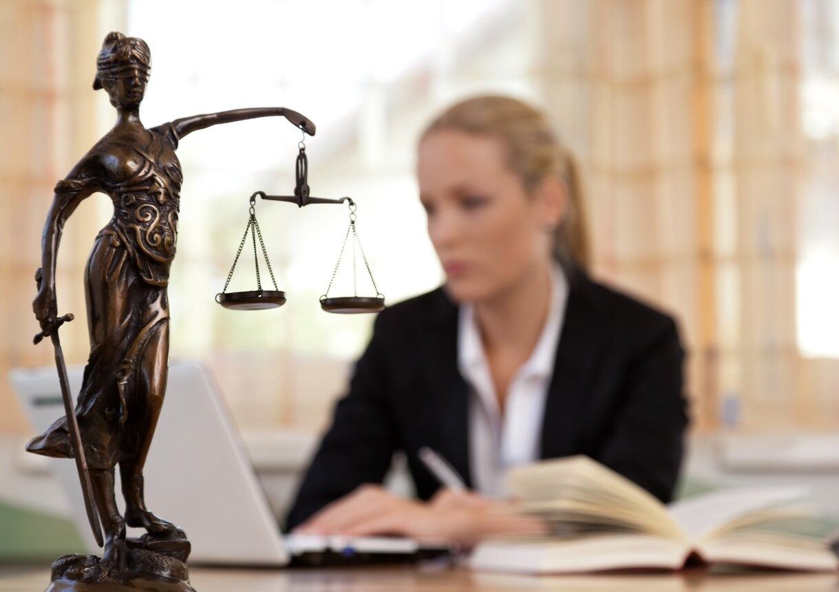 Estatua de Lady Justice, mujer de traje trabajando en un escritorio con una computadora portátil y un libro abierto.