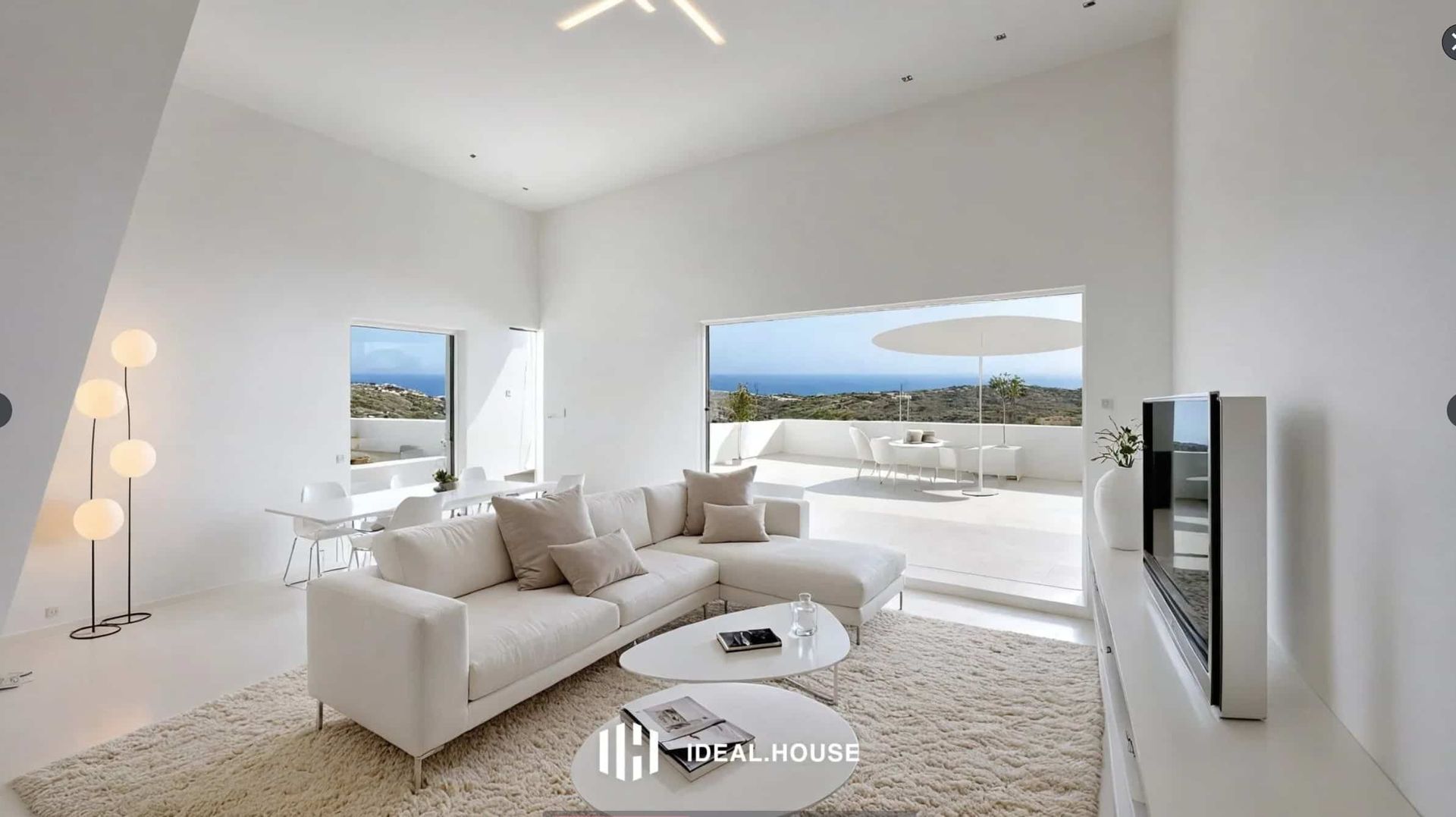 Sala de estar blanca brillante con sofá, mesas de café y vista al patio al aire libre y al océano.