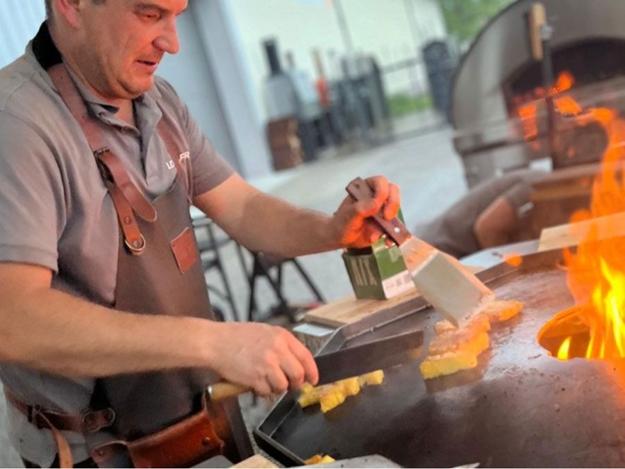 Mann grillt Essen auf einem großen Flachgrill, Flammen sichtbar, trägt eine Schürze.