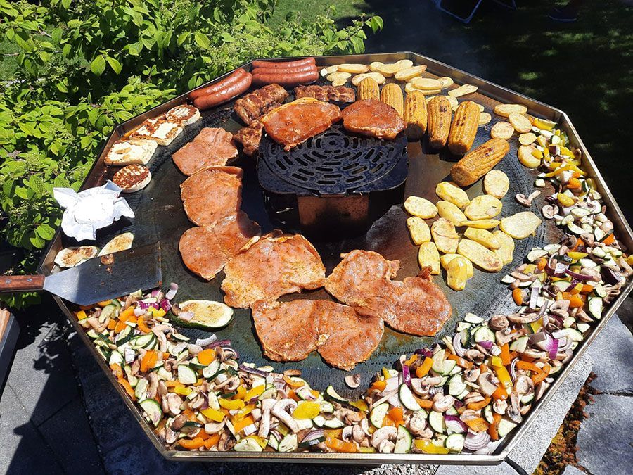 Large octagonal outdoor grill with assorted meats and vegetables cooking.