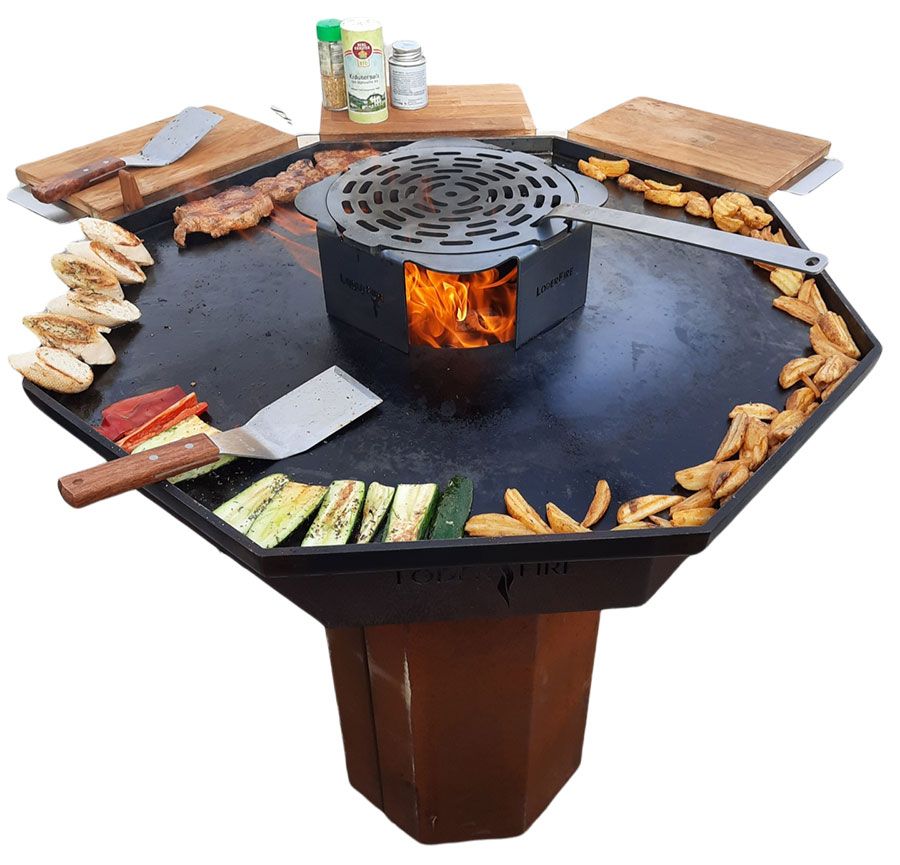 Achteckiger Außengrill mit Grillgut auf einer flachen Oberfläche, zentralem Feuer und seitlichen Schneidebrettern.