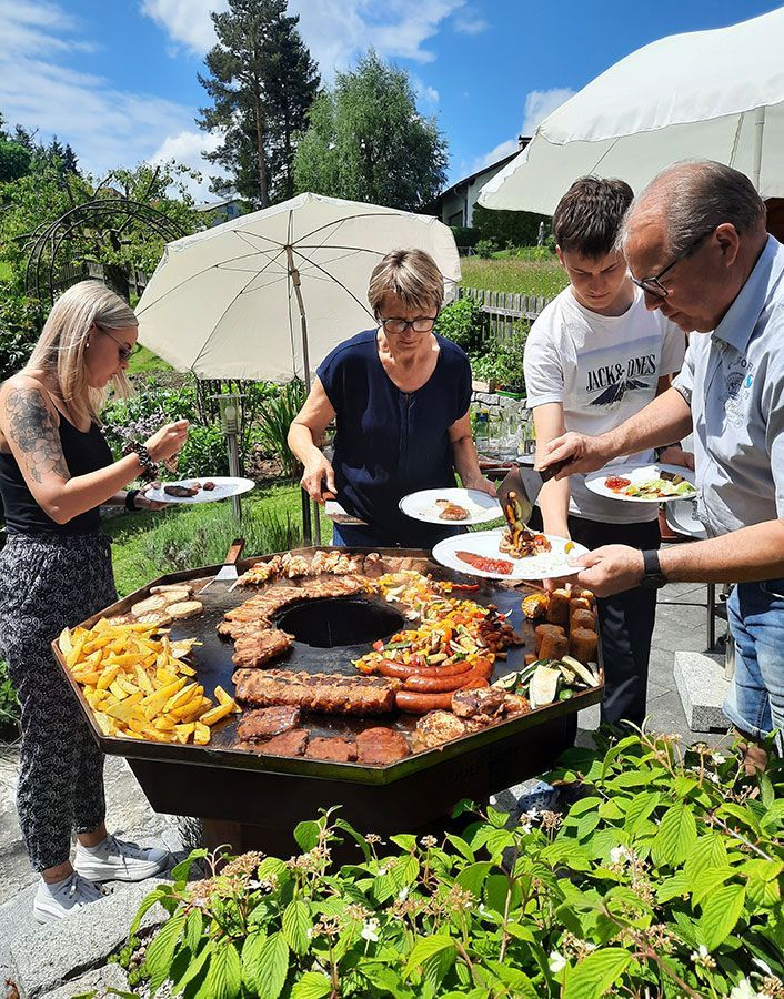 Group of people at an outdoor barbecue, serving food from a large grill.