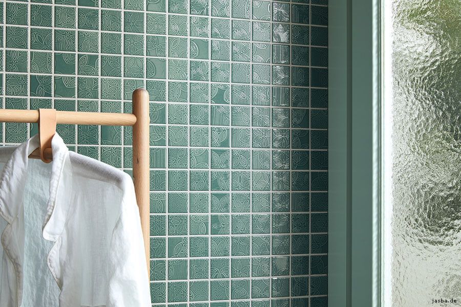Vor einer grün gefliesten Wand hängt ein weißes Hemd auf einem Ständer.