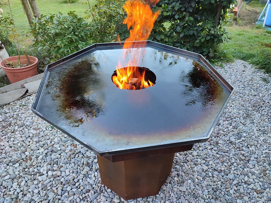 Feuerstelle mit Flammen und Kochfläche auf einer Steinterrasse.