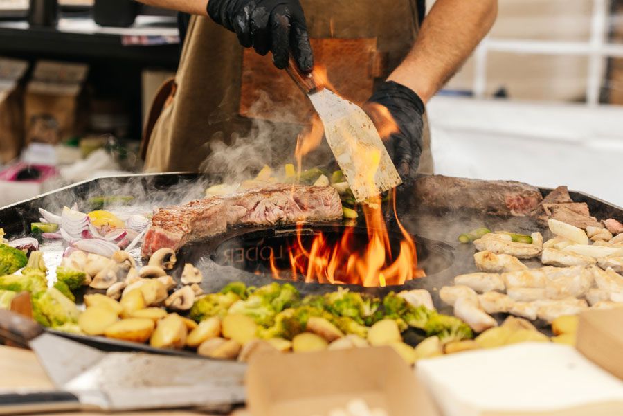 Koch grillt Fleisch und Gemüse über offenem Feuer an einem Imbissstand im Freien.
