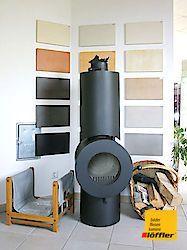 In einer Zimmerecke steht neben einem Korb mit Holzscheiten ein schwarzer Kamin.