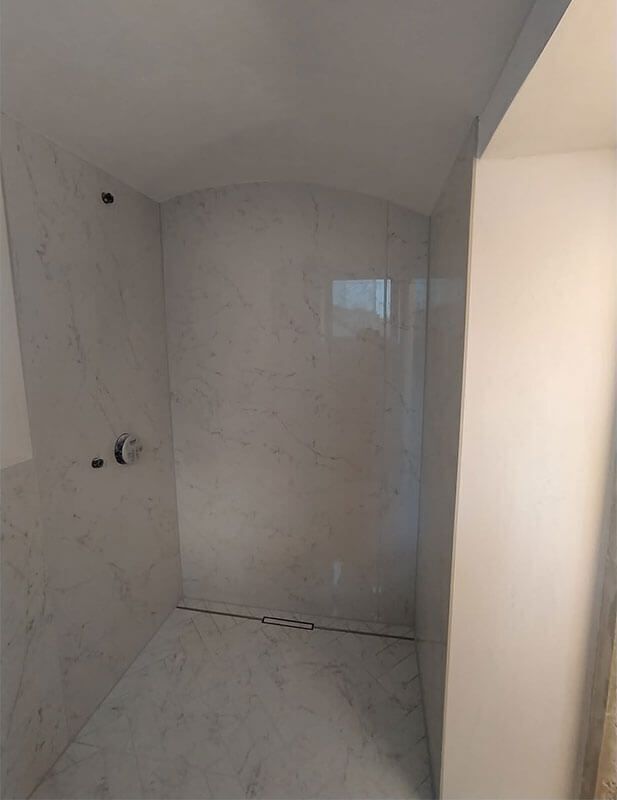 Ein Badezimmer mit weißen Fliesen und einer ebenerdigen Dusche.