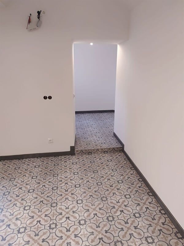 Ein leerer Raum mit gemustertem Boden und einer Tür, die zu einem anderen Raum führt.