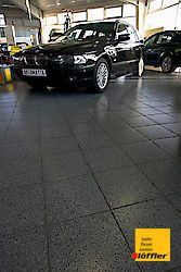 Ein schwarzes Auto steht in einem Ausstellungsraum mit gefliestem Boden.