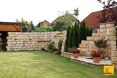 Eine Backsteinmauer umgibt einen üppigen grünen Rasen in einem Hinterhof.