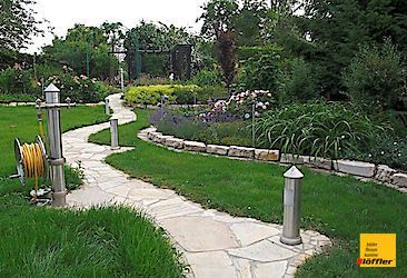 Ein Schlauch liegt am Rand eines Weges in einem Garten.