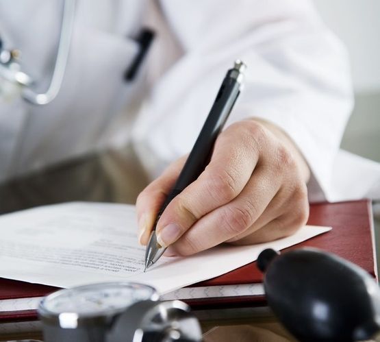 Un médico está escribiendo en un trozo de papel con un bolígrafo.