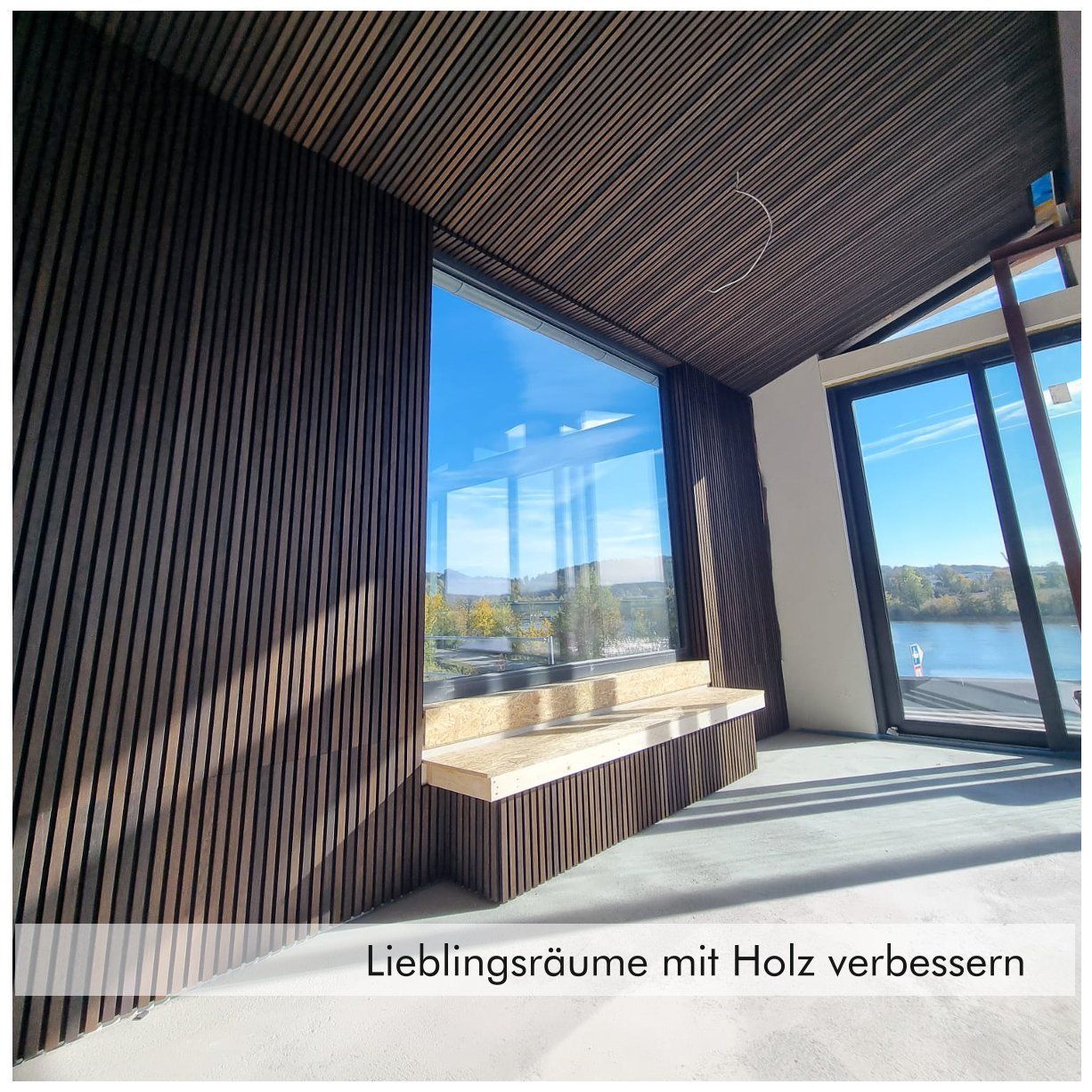 Raum mit großen Fenstern, einer Sitzecke unterm Fenster und schmalen Holzpaneelen an Wänden und Decke