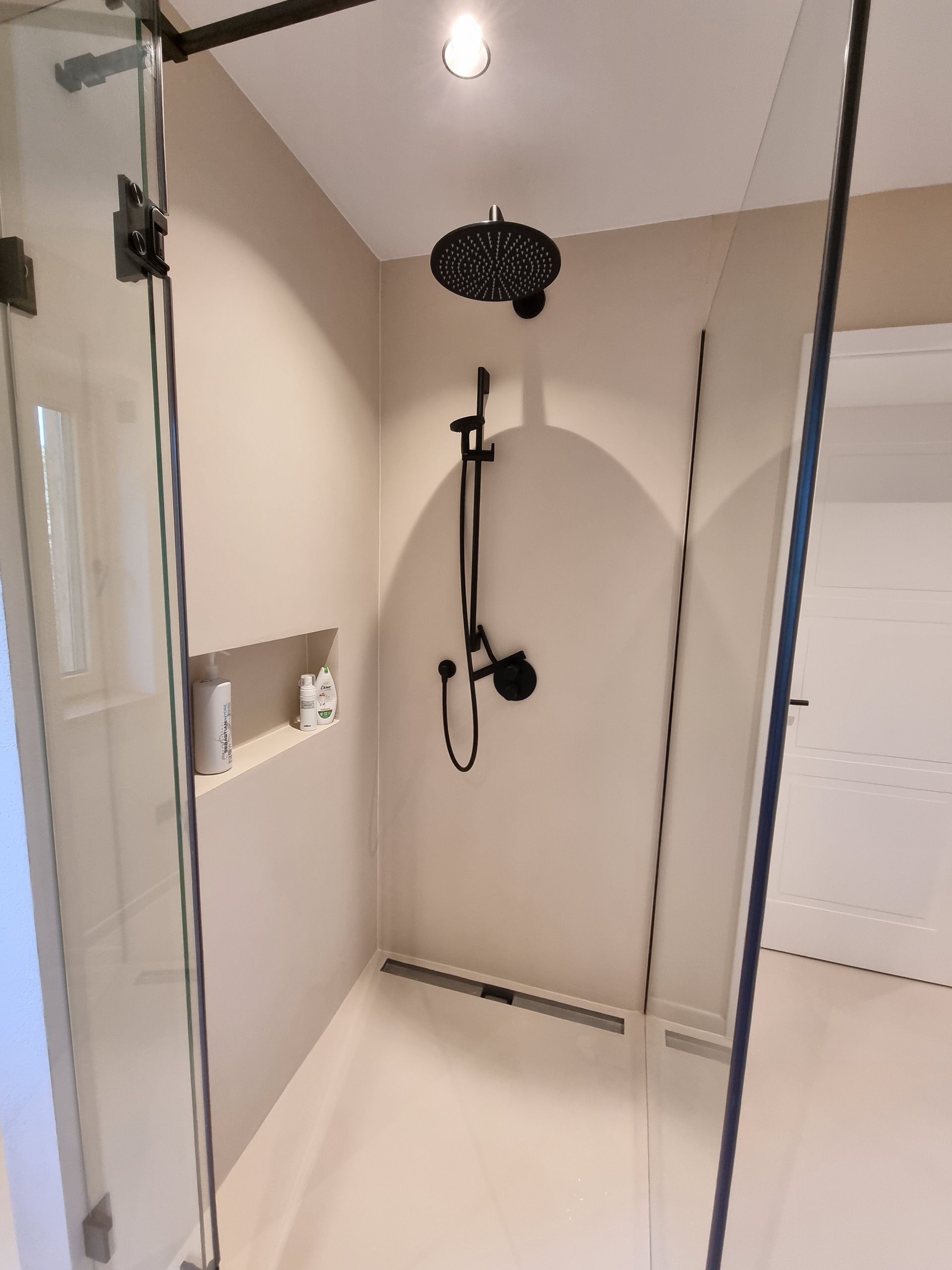 Nahaufnahme der ebenerdigen Dusche mit in der Wand eingelassenem Regal und schwarzen Armaturen 