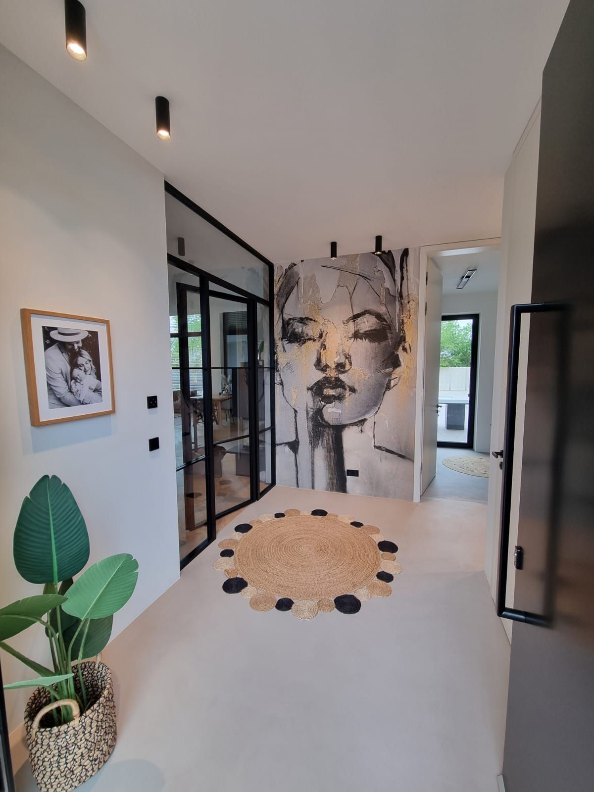 Modern eingerichteter Flur, Glastüren mit schwarzem Rahmen und abstrakter Fototapete einer Frau in Schwarz, Weiß und Gold