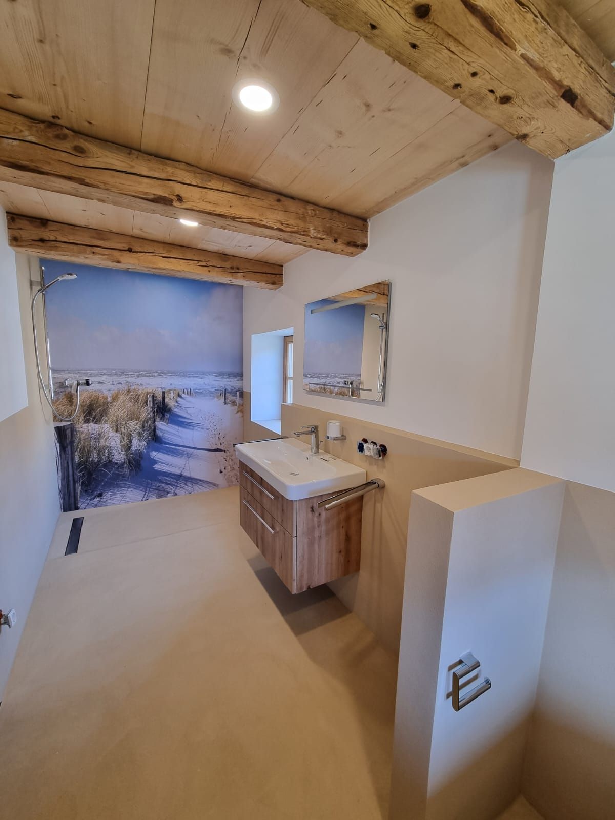 Badezimmer im Nordsee-Stil in weiß-beige Tönen, Holzbalken an der Decke und einer Dünen-Fototapete in der offenen Dusche