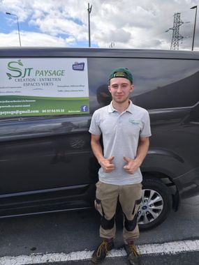 À l'extérieur, une personne en tenue de travail et coiffée d'un chapeau se tient devant une camionnette sombre portant le logo SJT PAYSAGE.