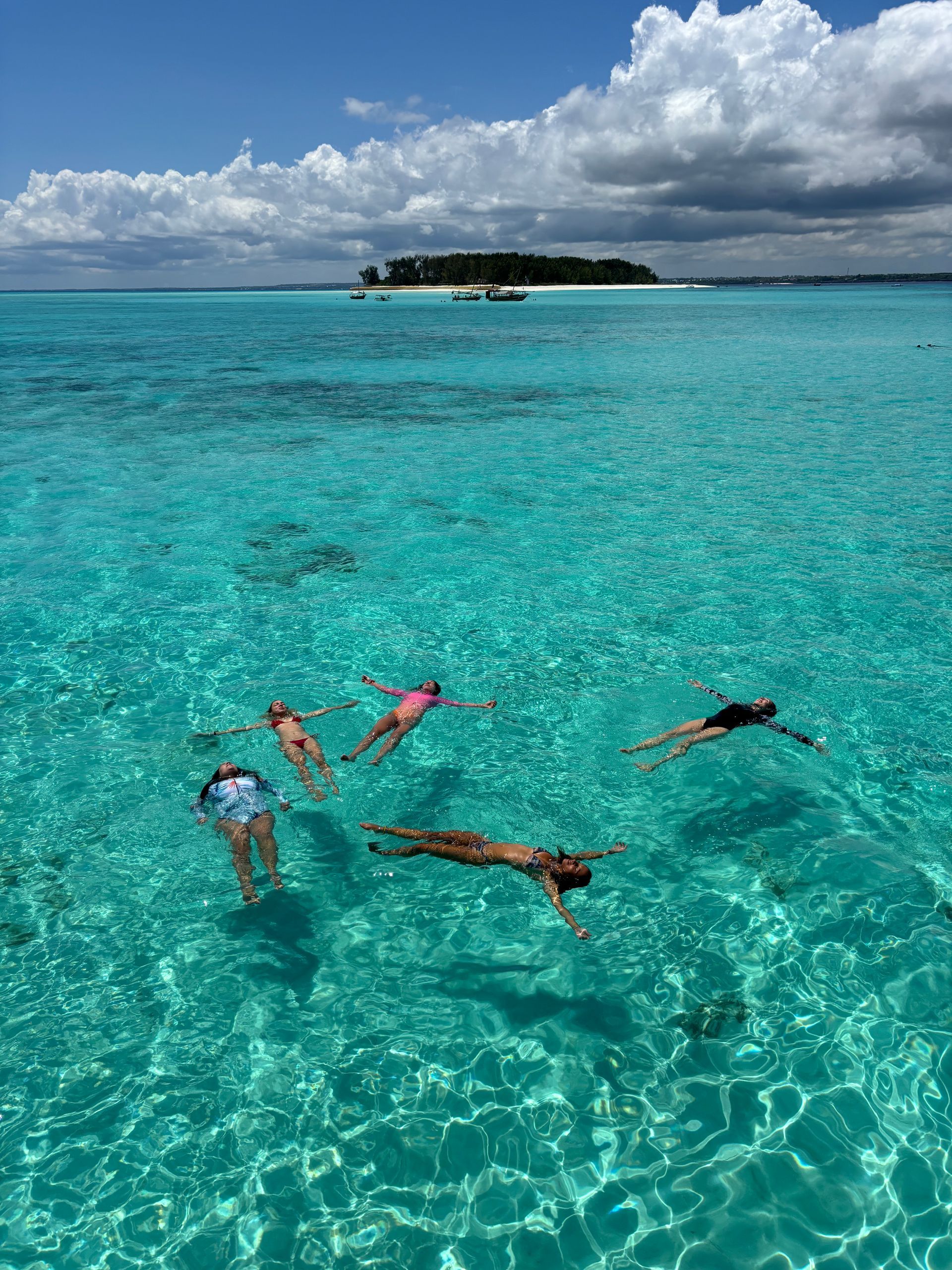Personas flotando en agua turquesa, una isla al fondo bajo un cielo azul con nubes.