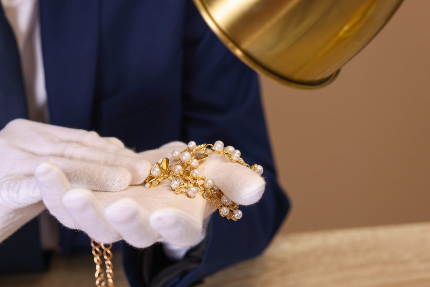 Manos enguantadas sosteniendo un collar de cadena de oro bajo una lámpara de aumento en un taller de joyería.