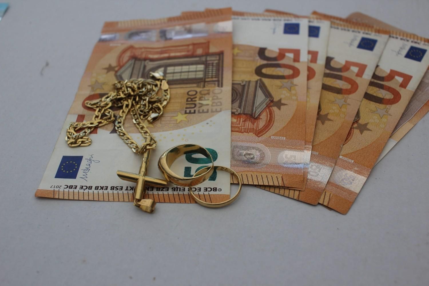 Billetes de euro con una cadena de joyería de oro y un colgante sobre una superficie clara.