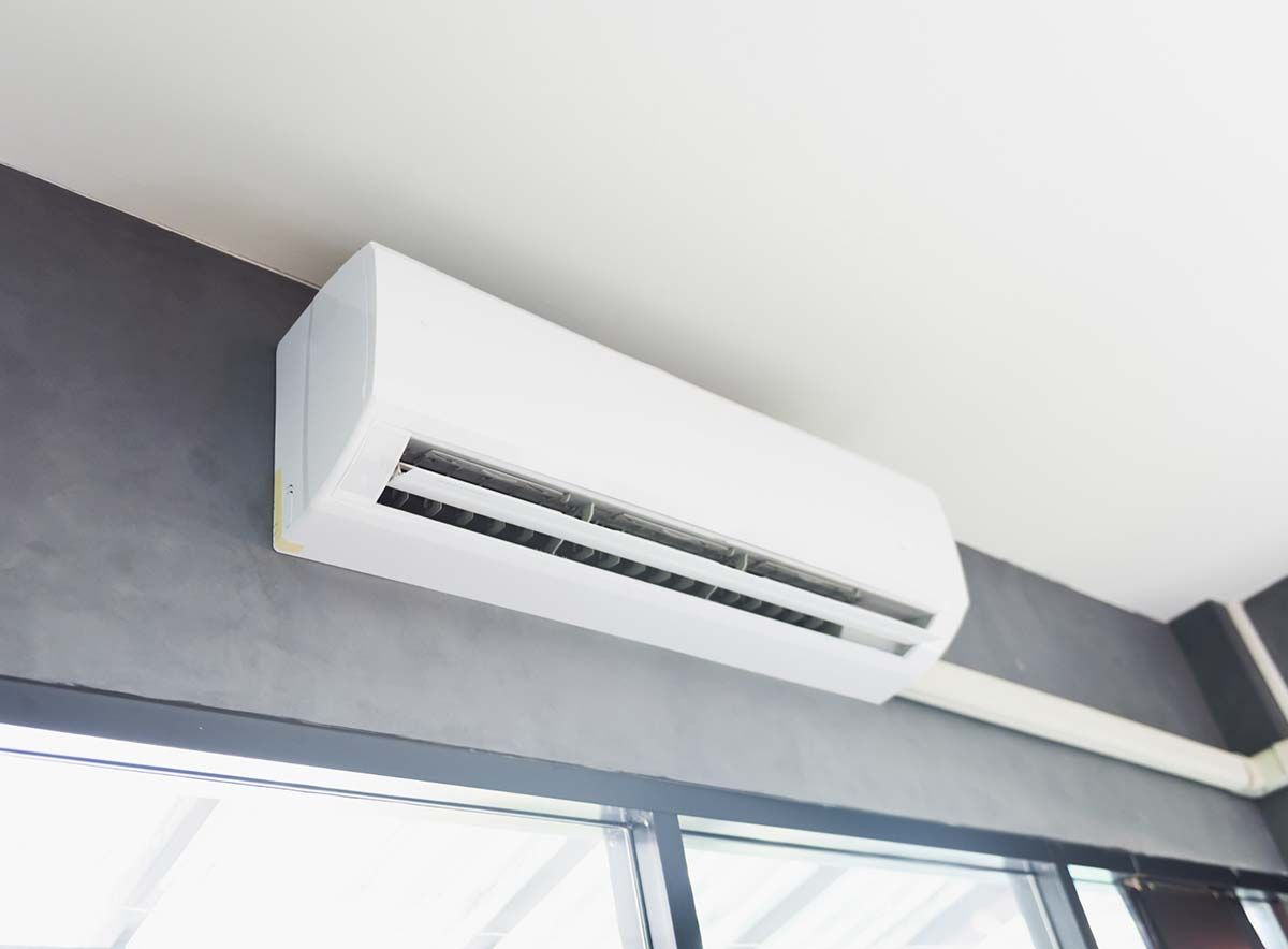 Un acondicionador de aire blanco cuelga del techo en una habitación al lado de una ventana.