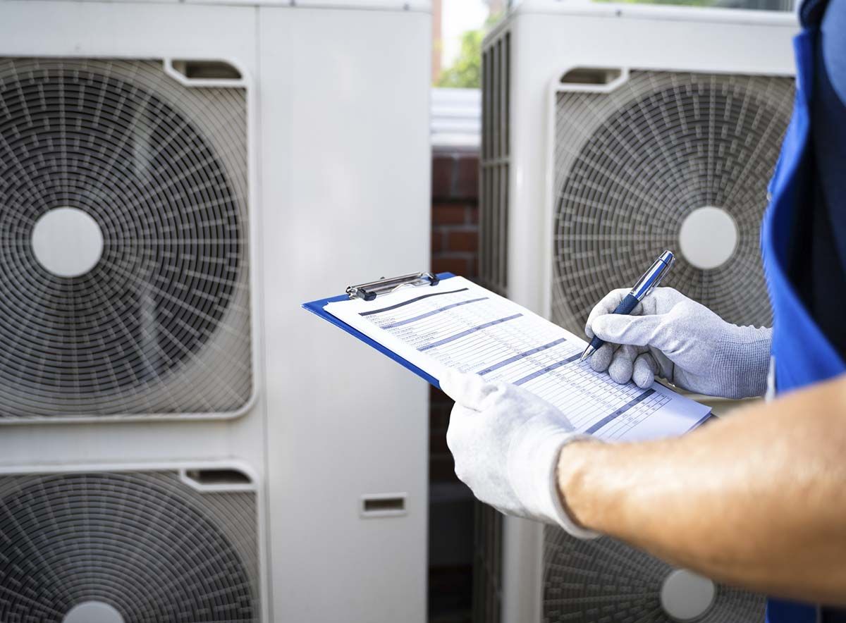 Un hombre escribe en un portapapeles frente a los acondicionadores de aire.