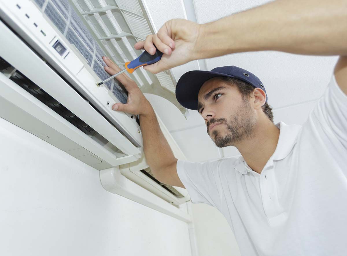 Un hombre está arreglando un aire acondicionado con un destornillador.