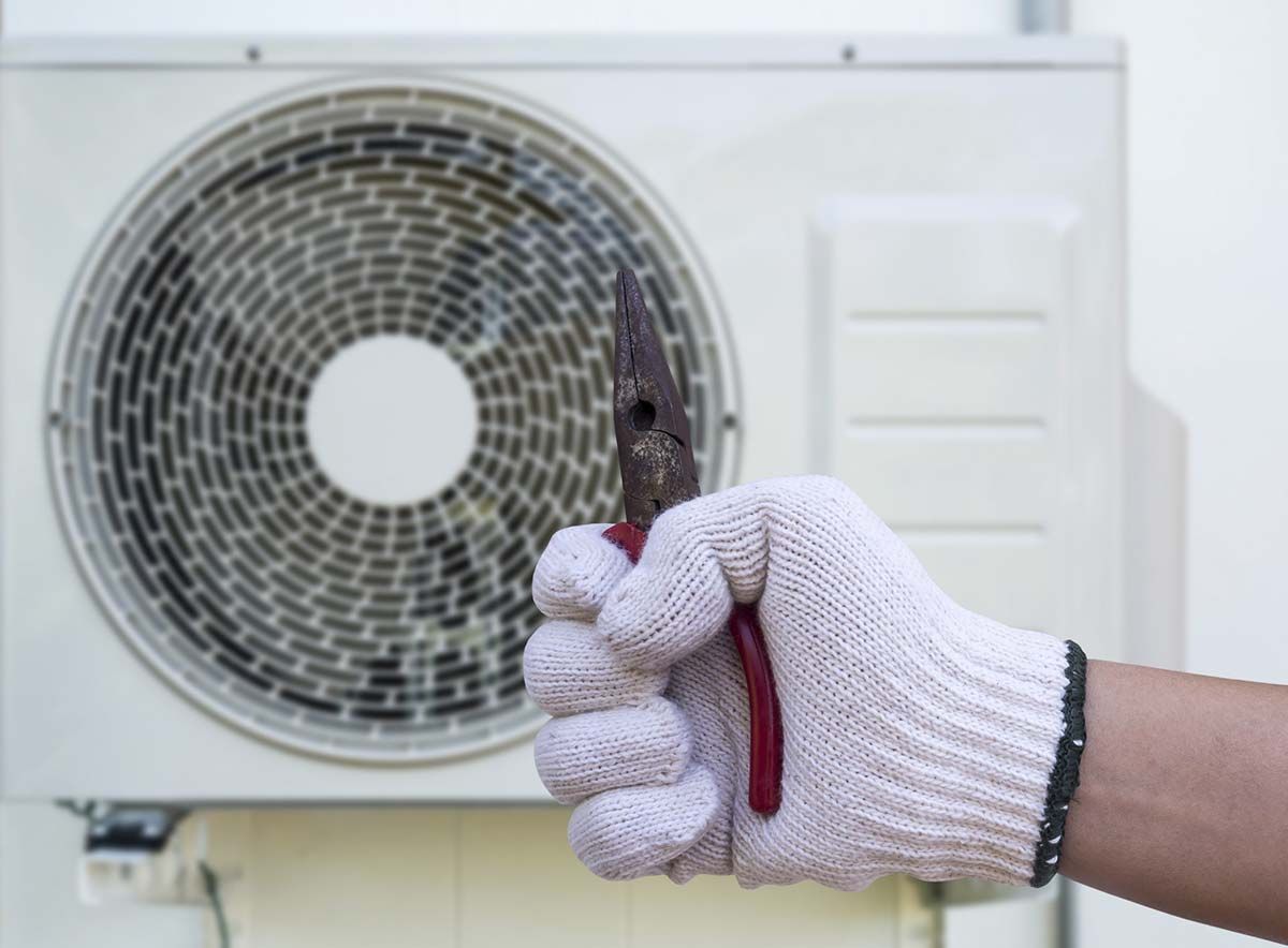 Una persona sostiene un par de alicates frente a un acondicionador de aire.