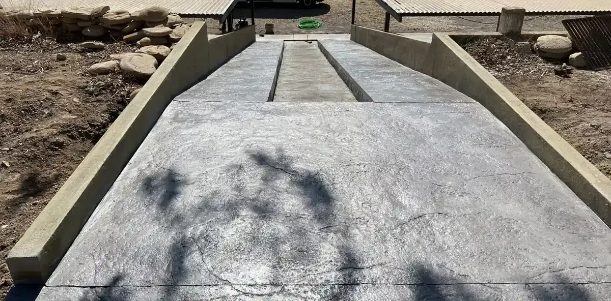 Rampa de hormigón con muros laterales elevados que conduce a una estructura. Sombra de algo sobre ella.