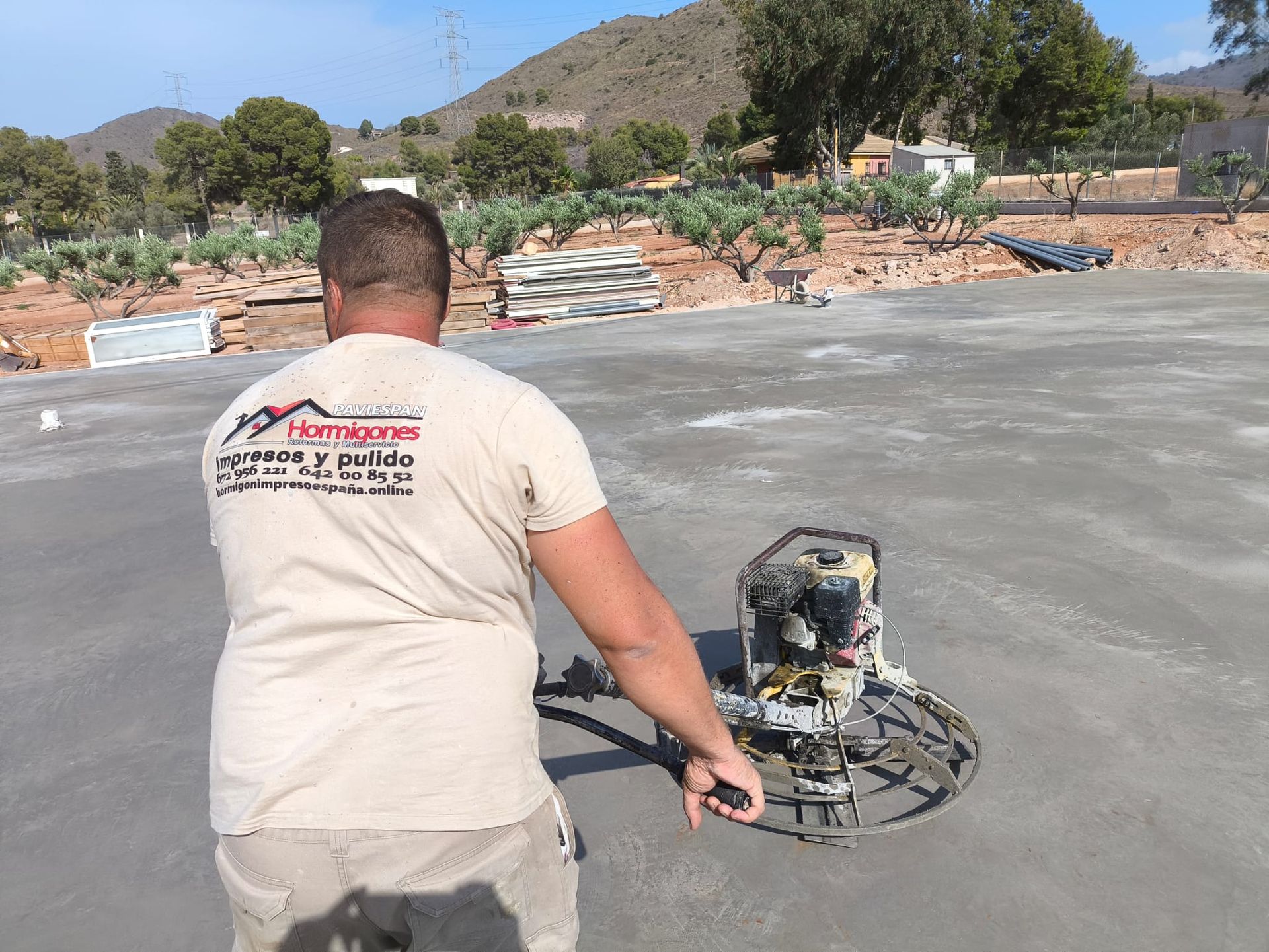 Hombre operando una máquina de acabado de hormigón sobre una superficie de hormigón recién vertida al aire libre.